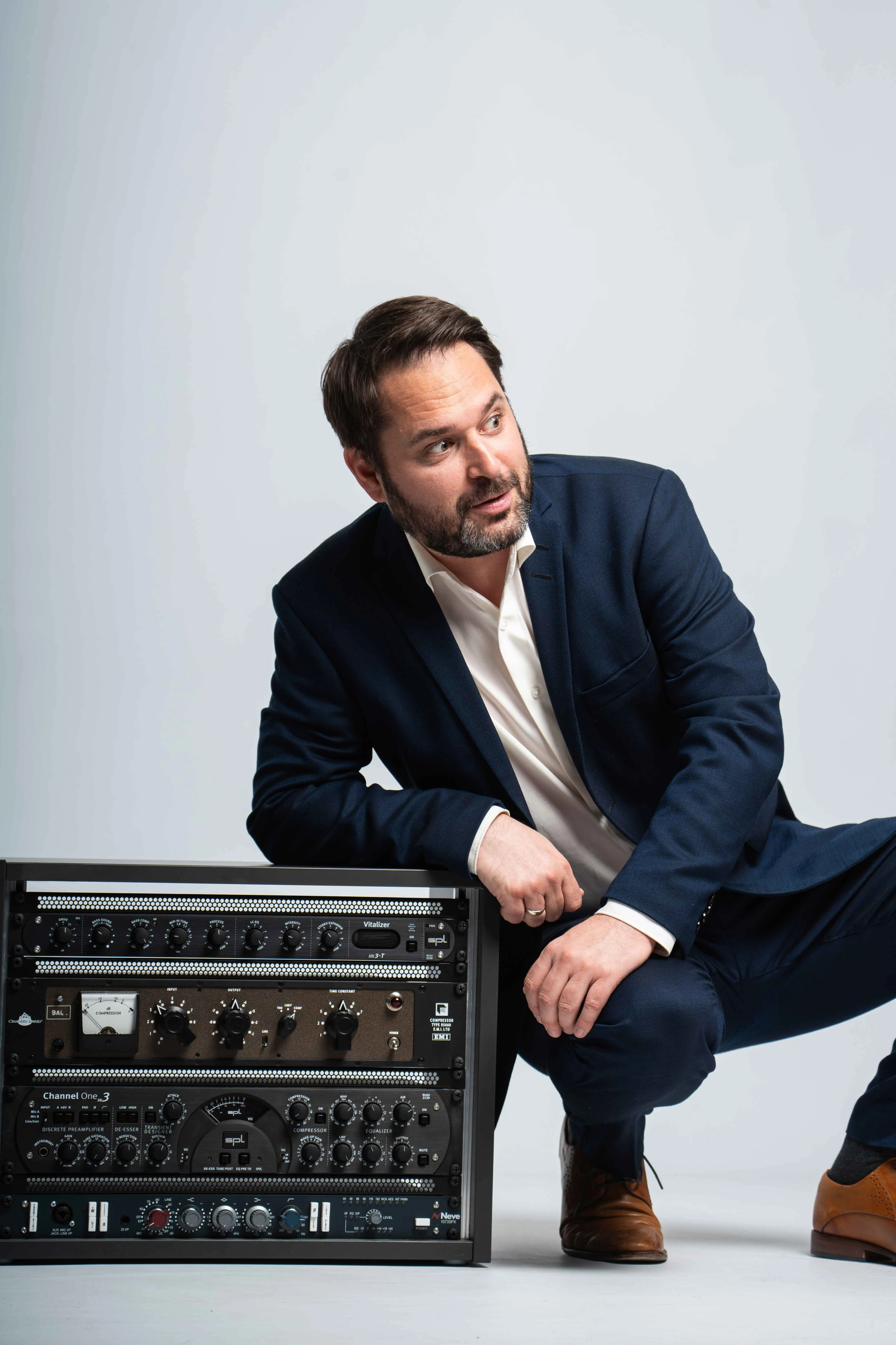 Christian Grollmann hockt im Studio neben einem 19-Zoll-Rack mit analogen Audio-Prozessoren und schaut konzentriert zur Seite.