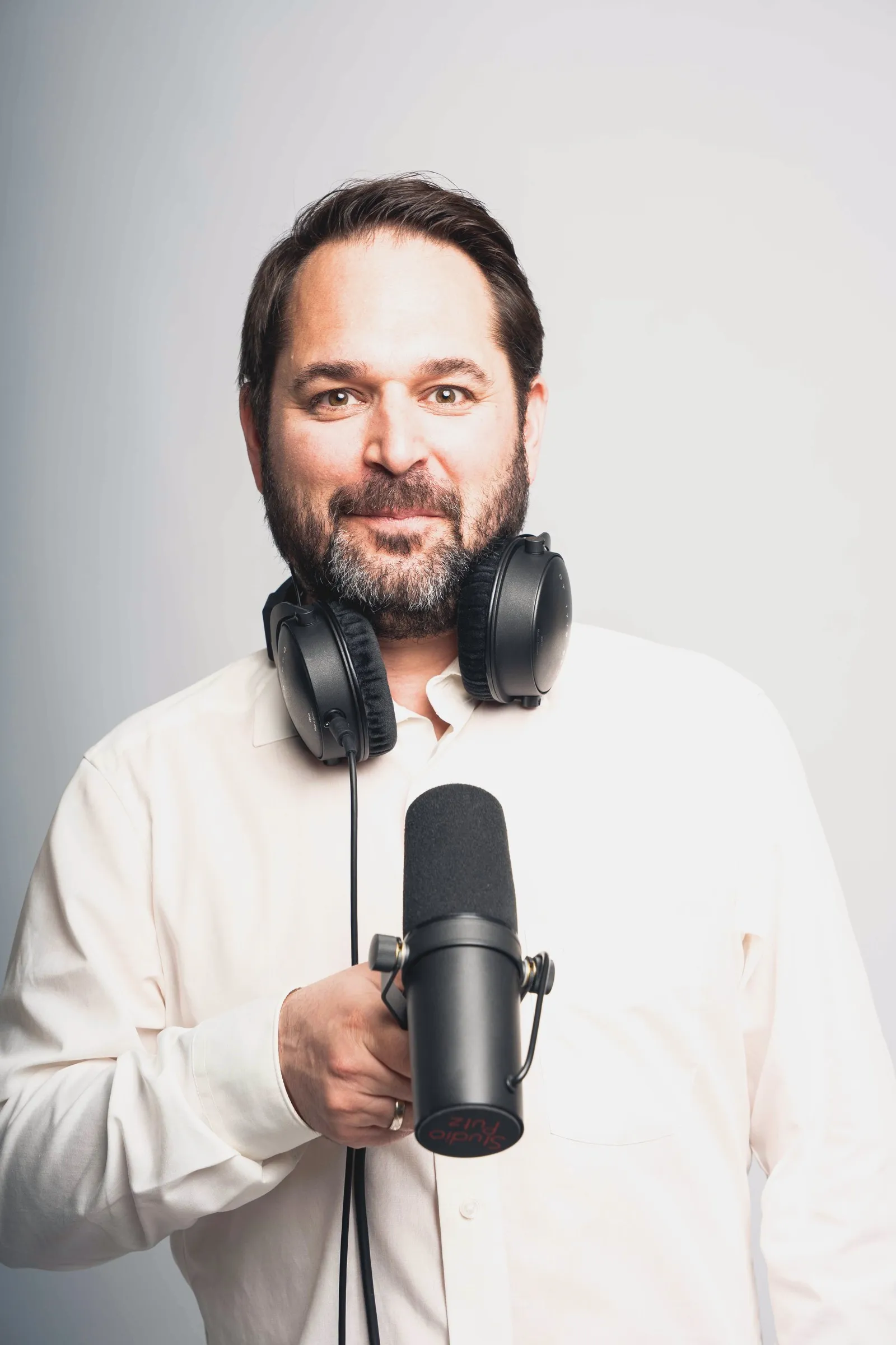 Martin Putz lächelt in die Kamera, um den Hals einen Kopfhörer, in der Hand ein Podcast-Mikrofon.