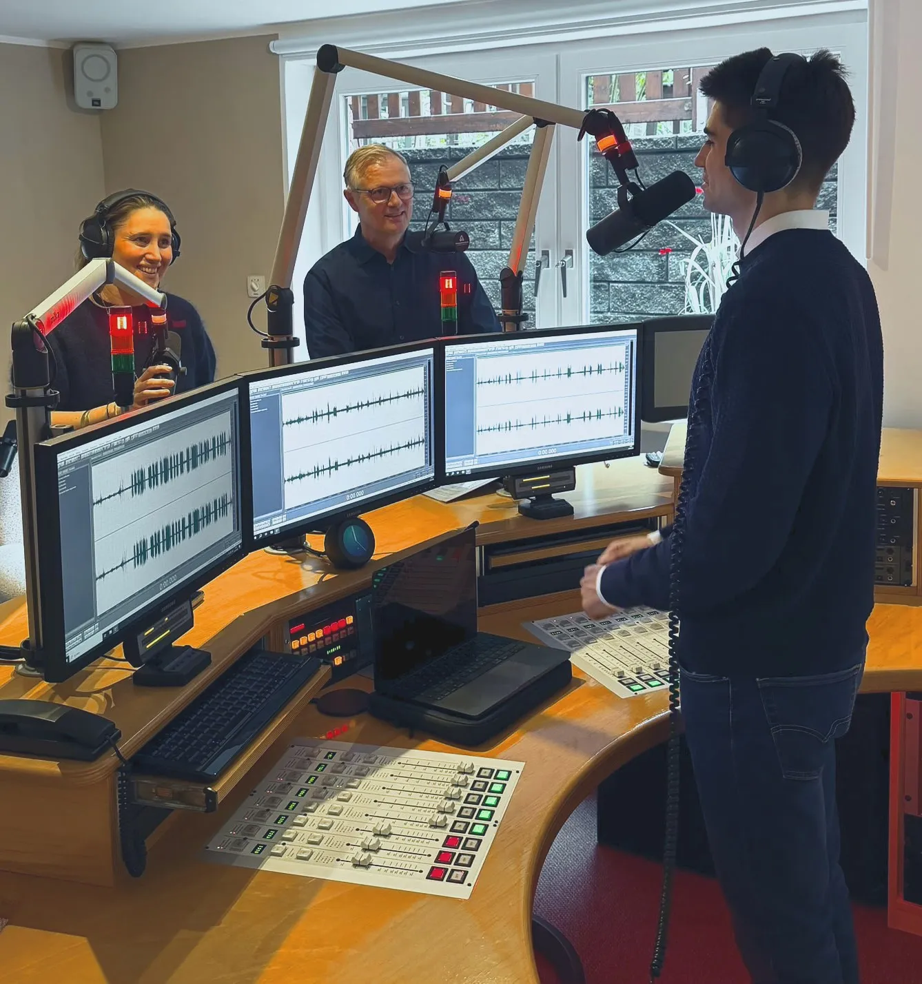 Drei Personen an Mikrofonen bei einer Podcast-Aufnahme in unserem Studio in Hamburg, davor Bildschirme mit Tonspuren und ein Mischpult